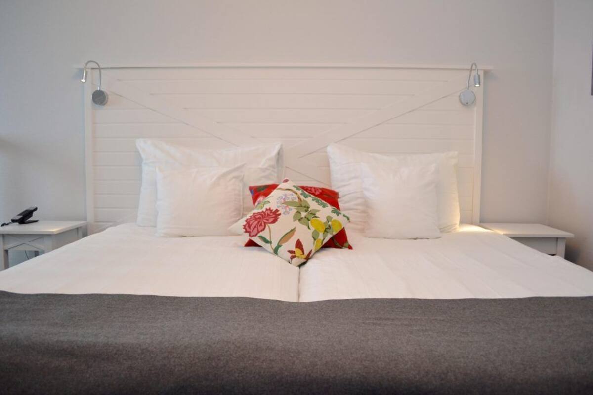 A neatly made bed with white linens and a grey throw blanket, two white pillows, and a single floral pillow on a white headboard.