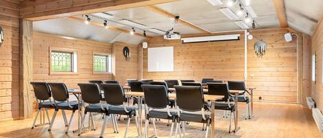 Un salón de conferencias con paredes de madera, un proyector y varias sillas dispuestas alrededor de una mesa.