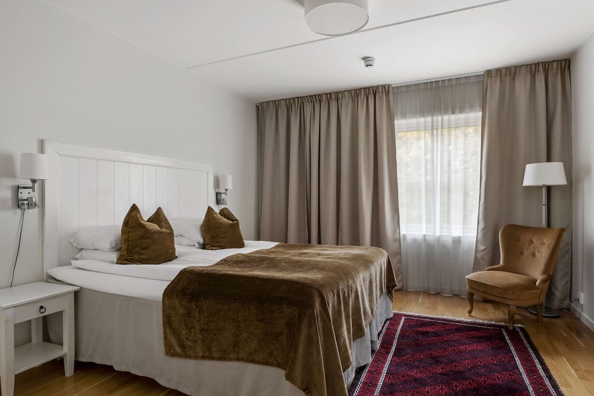 Een slaapkamer met een bed, een stoel, een nachtkastje en een raam met gordijnen.