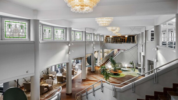 Eine geräumige Lobby mit Treppe, Sitzbereichen und großen Fenstern.