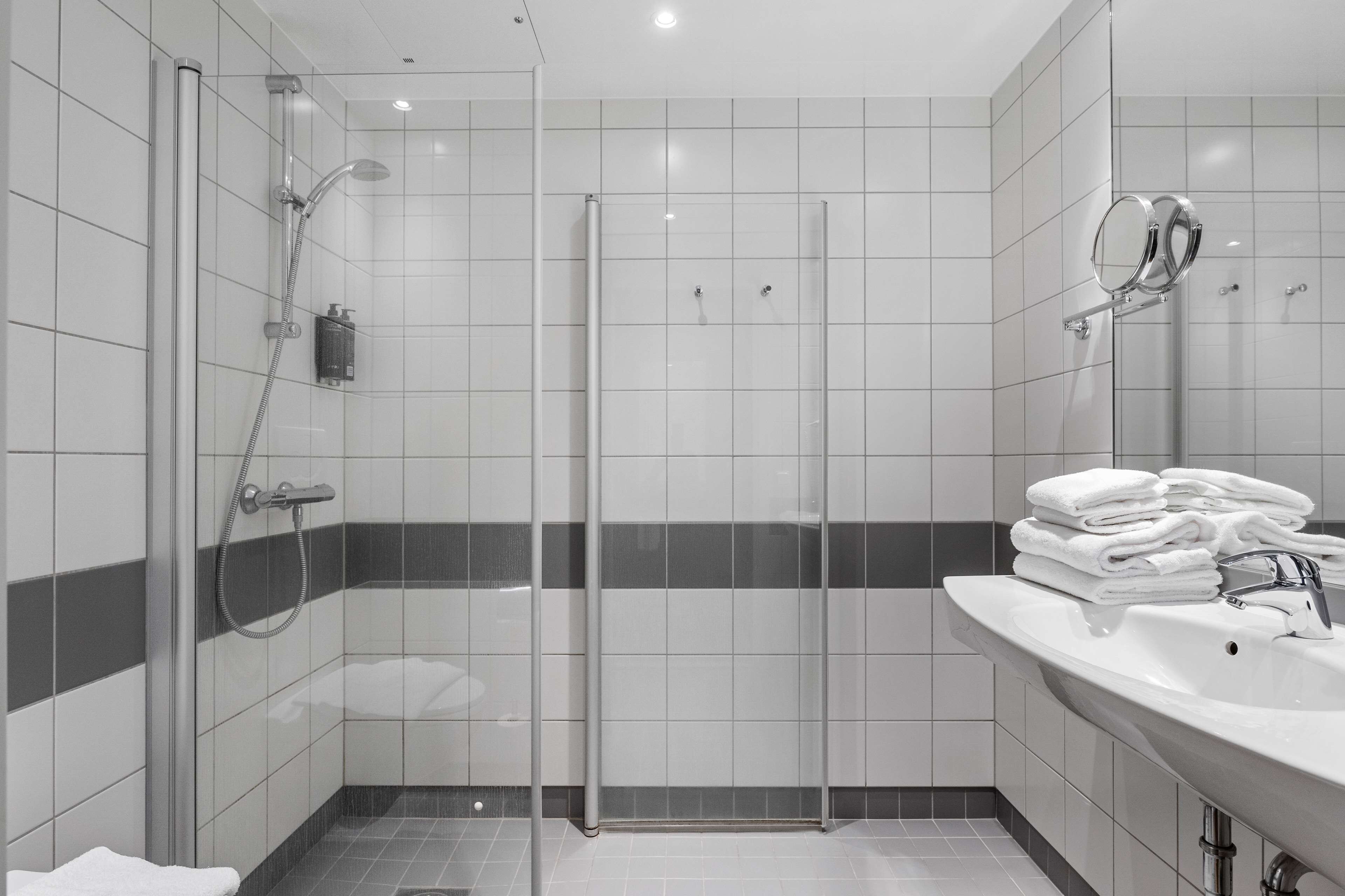 Ein modernes Badezimmer mit einer ein Glasfach raumbildenden Dusche, einem Waschbecken mit Spiegel und ordentlich gestapelten Handtüchern.