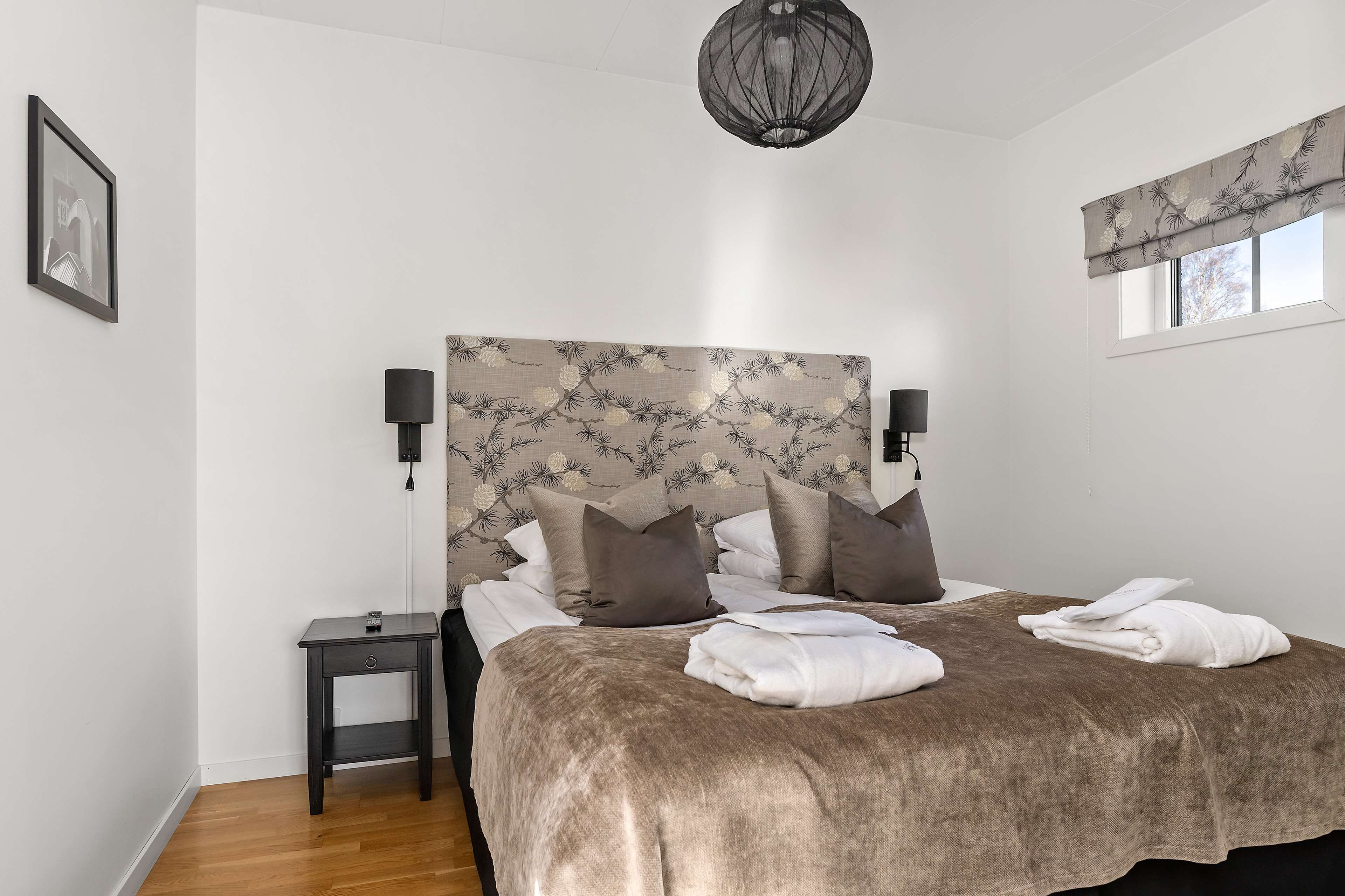 A bedroom with a large bed, a nightstand, a lamp, and a window with a valance.