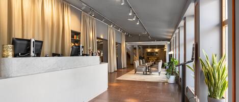 A hotel reception area with a marble counter, beige curtains, and a seating area with tables and chairs.