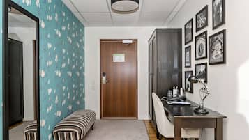A hallway with a wooden door, a bench, a desk with a lamp, and framed pictures on the wall.