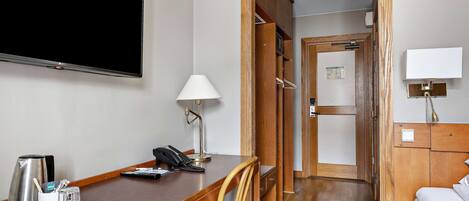 A hotel room with a wooden desk, a flat-screen TV, a lamp, a coffee maker, and a telephone.