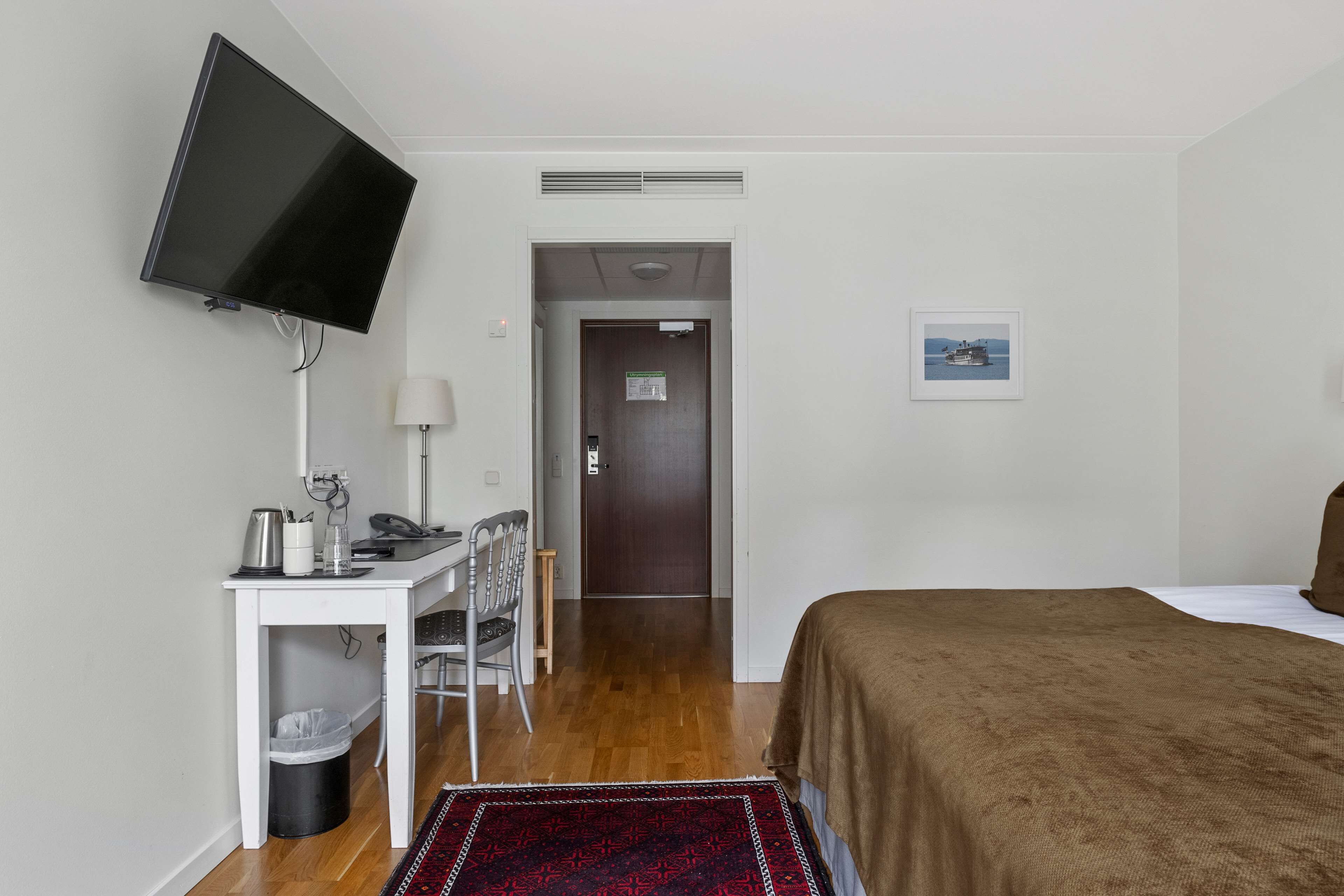 A hotel room with a bed, a desk with a chair, a television, and a door leading to another room.