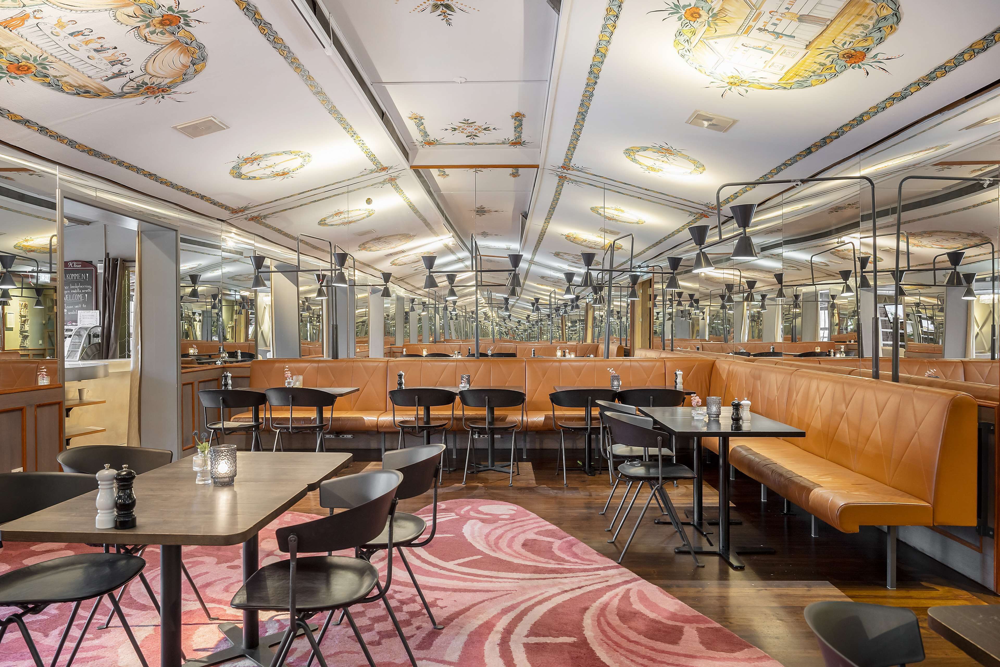 Un restaurante con techos altos, decoraciones ornamentales en el techo y una variedad de asientos, incluyendo cabinas y mesas.