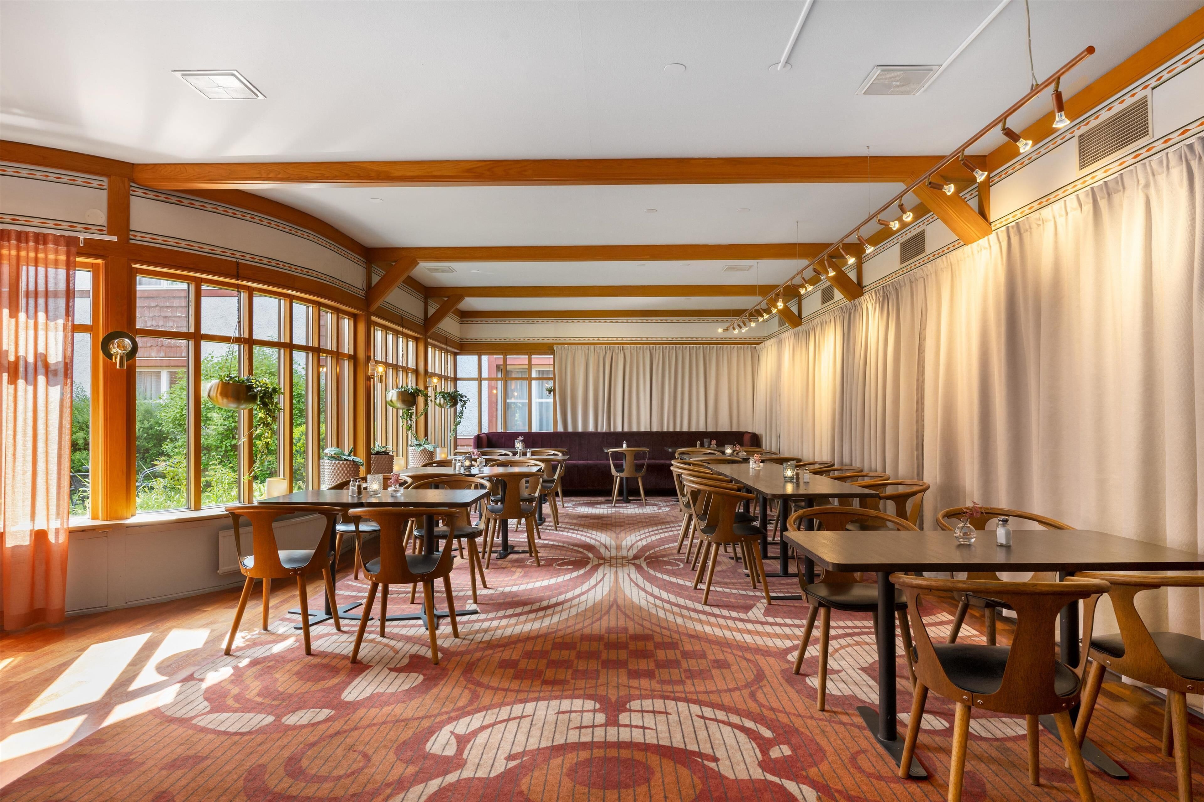 A spacious dining area with wooden tables and chairs, large windows, and a patterned carpet.