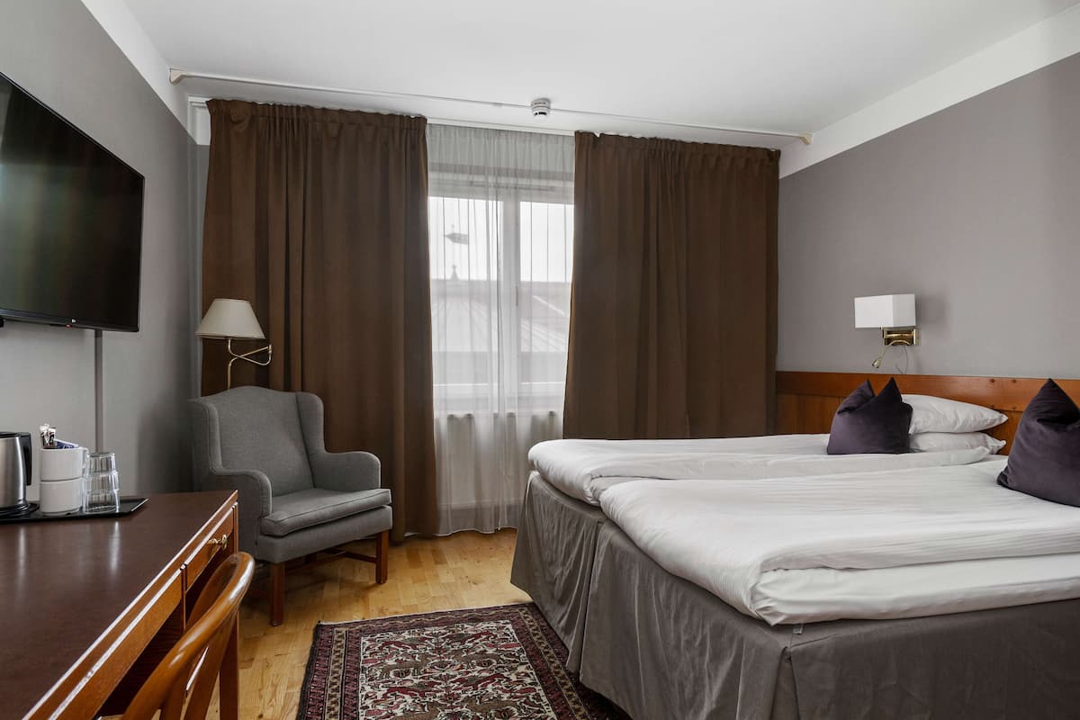 Een hotelkamer met een bed, een bureau, een stoel, een televisie en een raam met gordijnen.