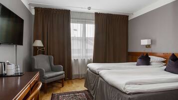 A hotel room with a bed, a desk, a chair, a TV, and a window with curtains.