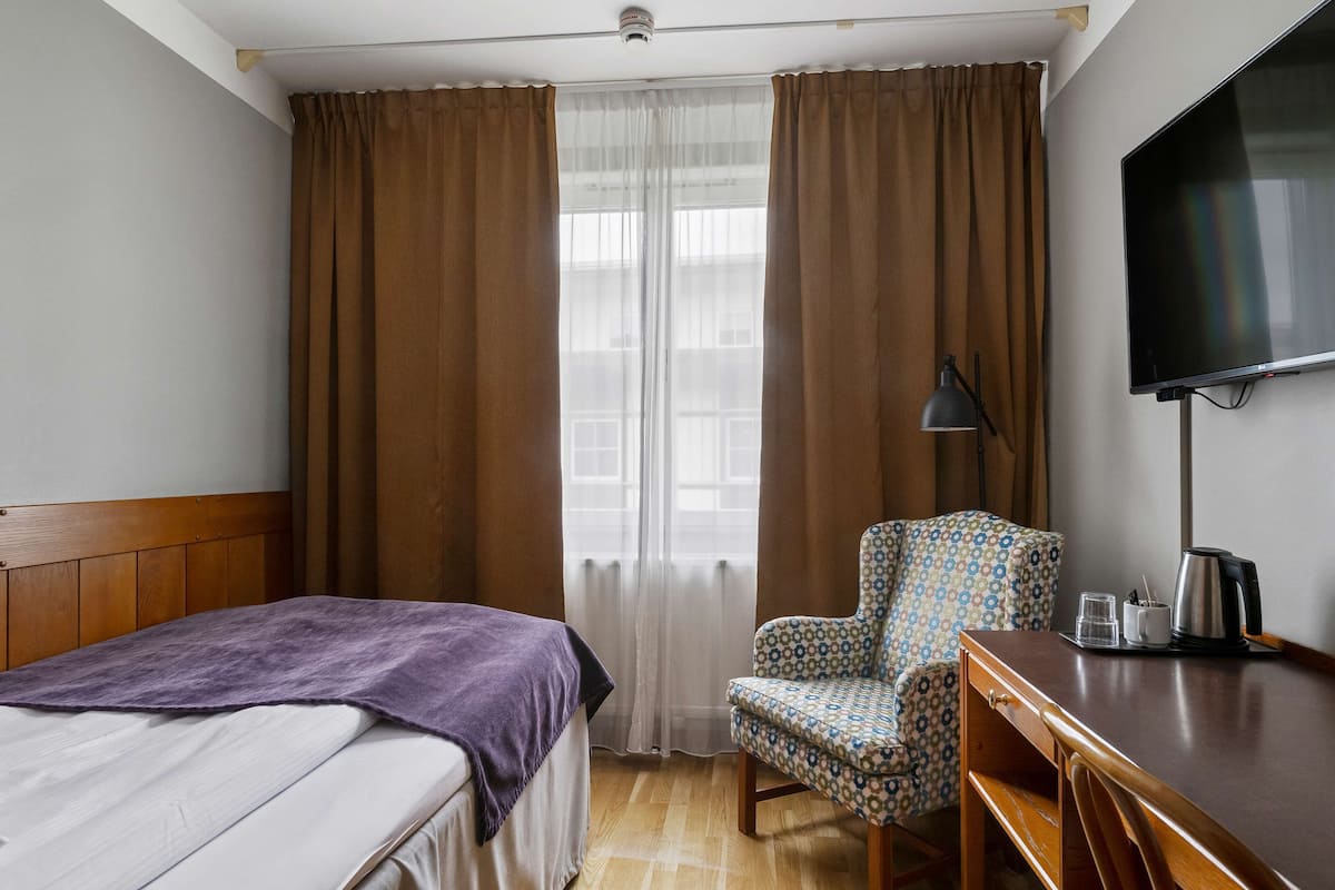 Een hotelkamer met een bed, een bureau, een stoel, een televisie en een raam met gordijnen.