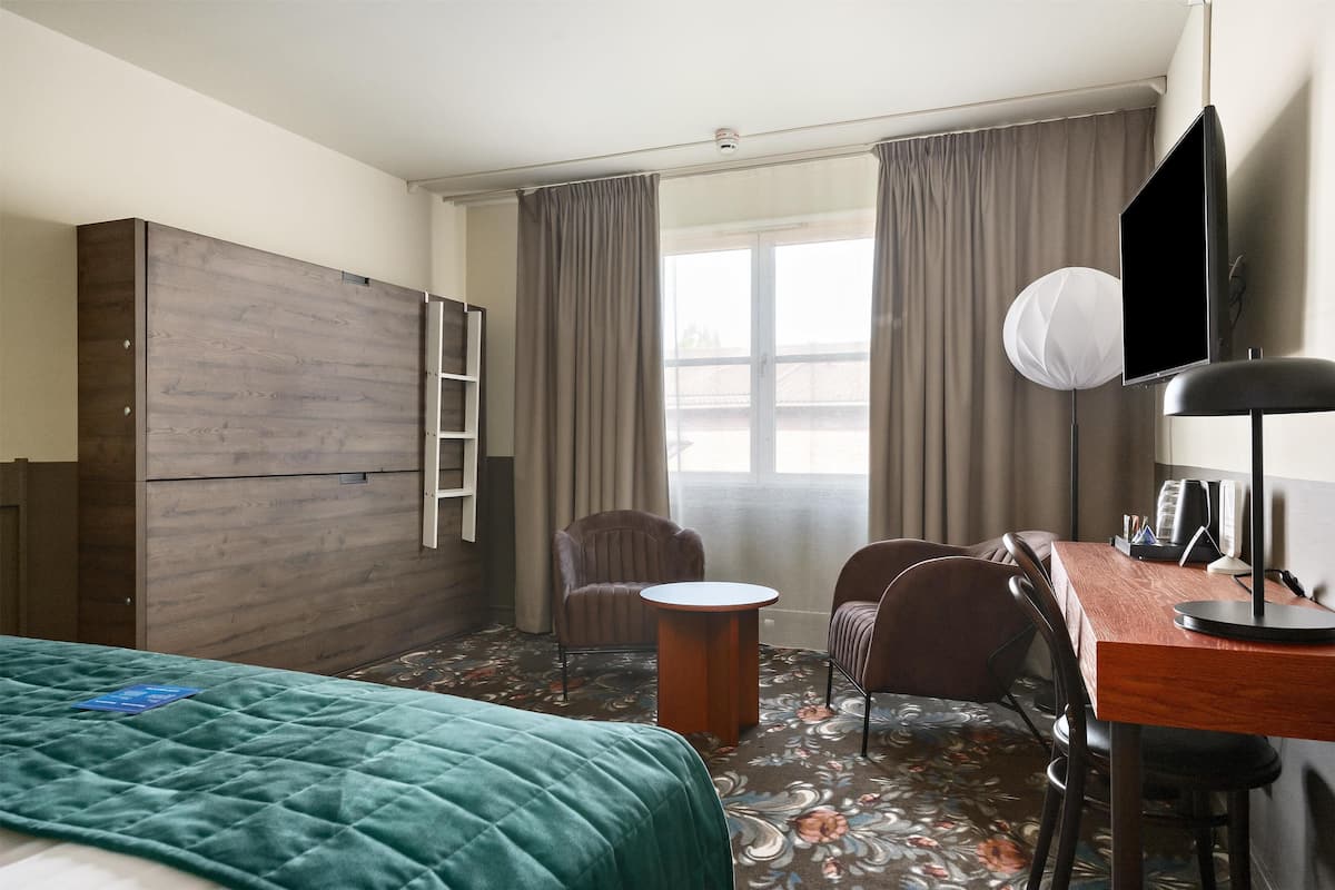 Een hotelkamer met een bed, bureau, stoel, kledingkast en raam met gordijnen.