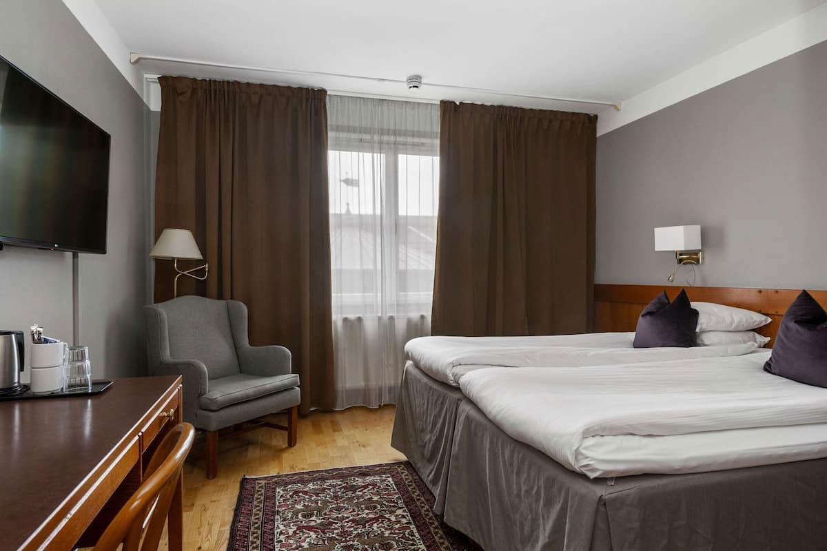 Een hotelkamer met een bed, een bureau, een stoel, een televisie en een raam met gordijnen.