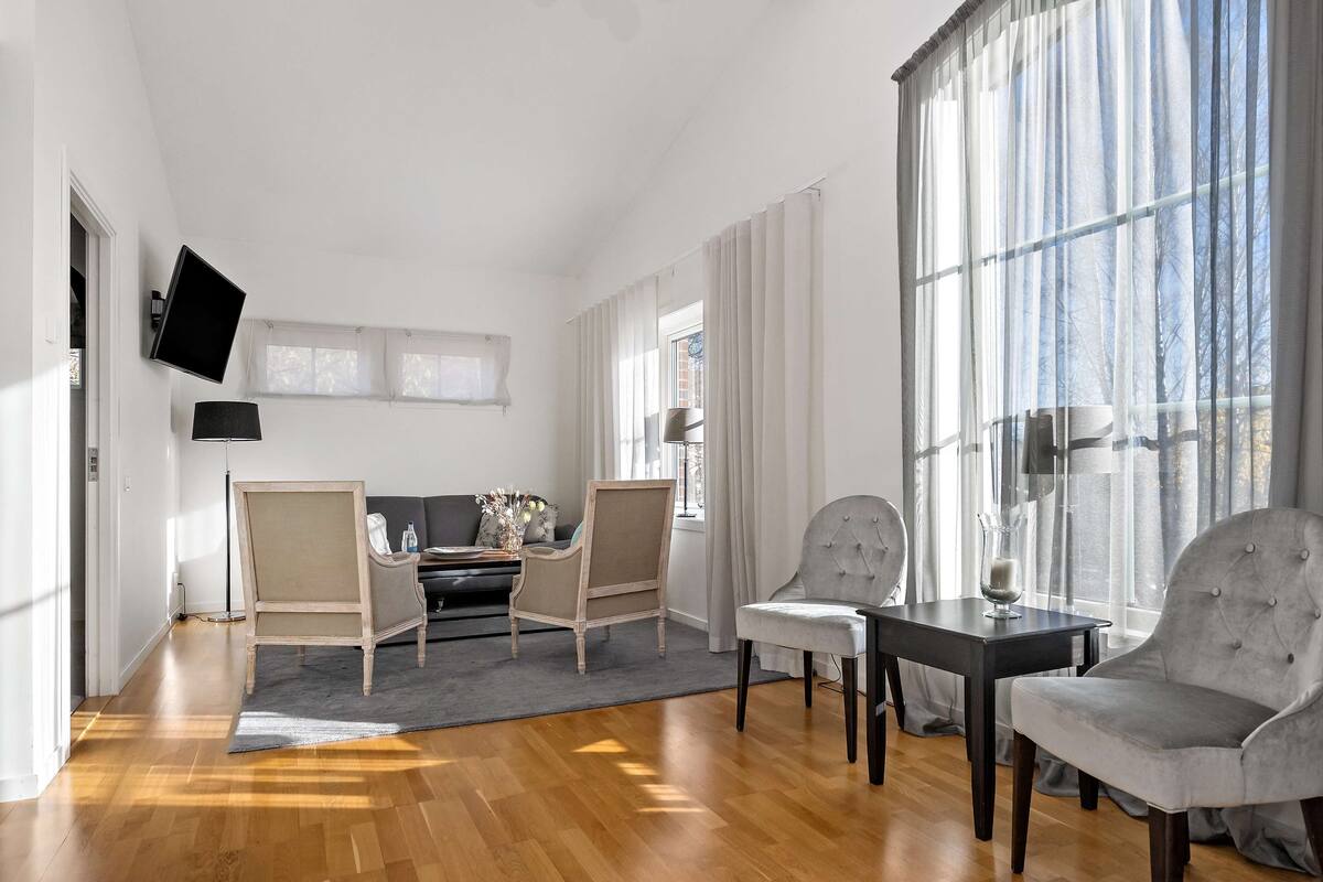 Een moderne woonkamer met een bank, twee fauteuils, een eettafel en een aan de muur bevestigde televisie.