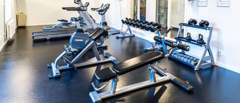 Un gimnasio con cintas de correr, una prensa de pesas, mancuernas y un reloj de pared.