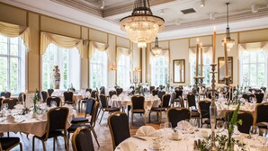 A banquet hall with round tables, chandeliers, and elegant table settings. - Grand Hotel Alingsås (Alingsas)