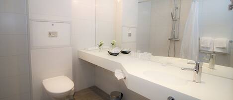 A modern bathroom with a white toilet, a large mirror, a sink with a chrome faucet, and a shower area.