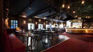 A restaurant with a bar area, multiple tables and chairs, and a red carpeted floor. - Grand Hotel Alingsås (Alingsas)