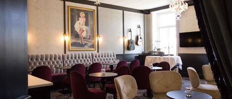 A restaurant with a tufted bench seating, round tables, and a chandelier.