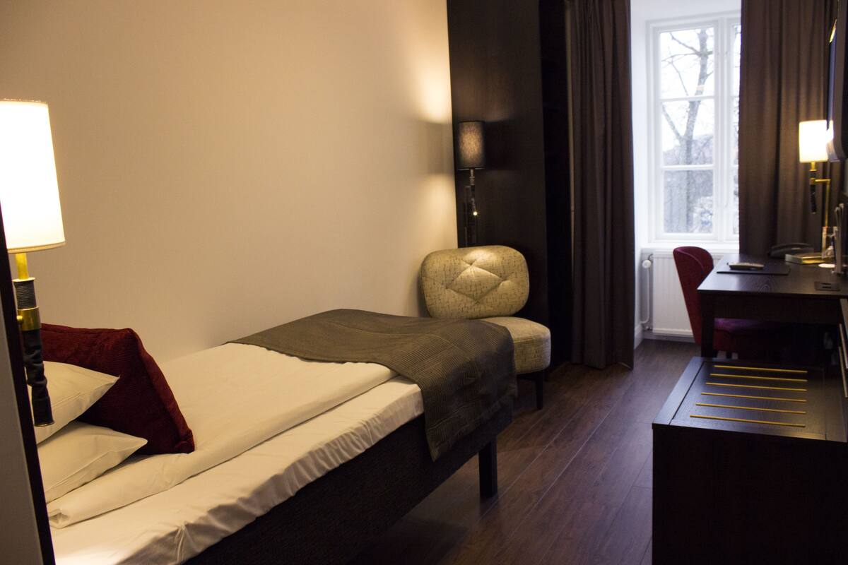 A small, neatly arranged bedroom with a single bed, a desk, and a chair.