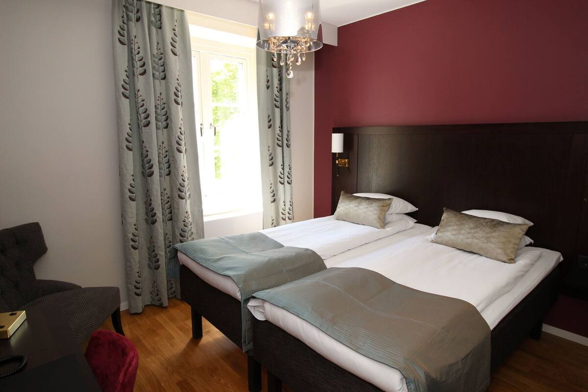 A double bed with two pillows, a bedside table, a chair, and a chandelier.