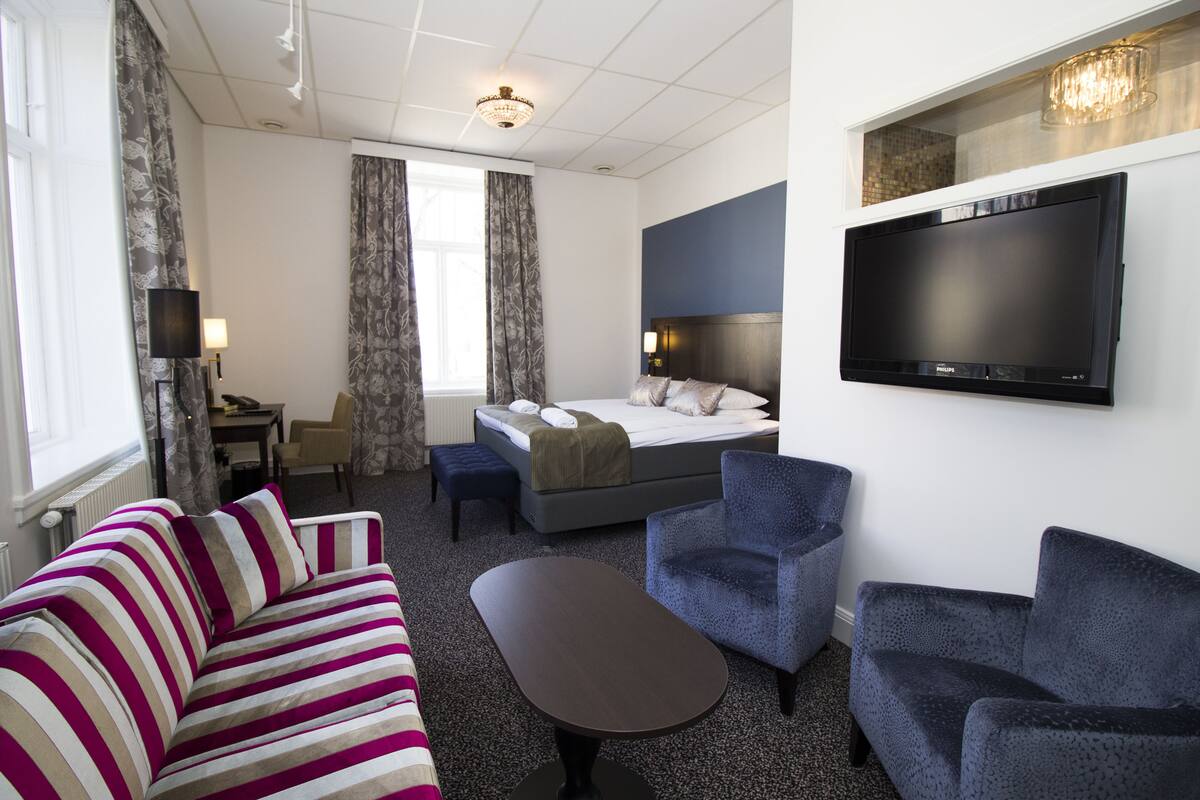 A hotel room with a bed, a TV, a sofa, a chair, and a desk.