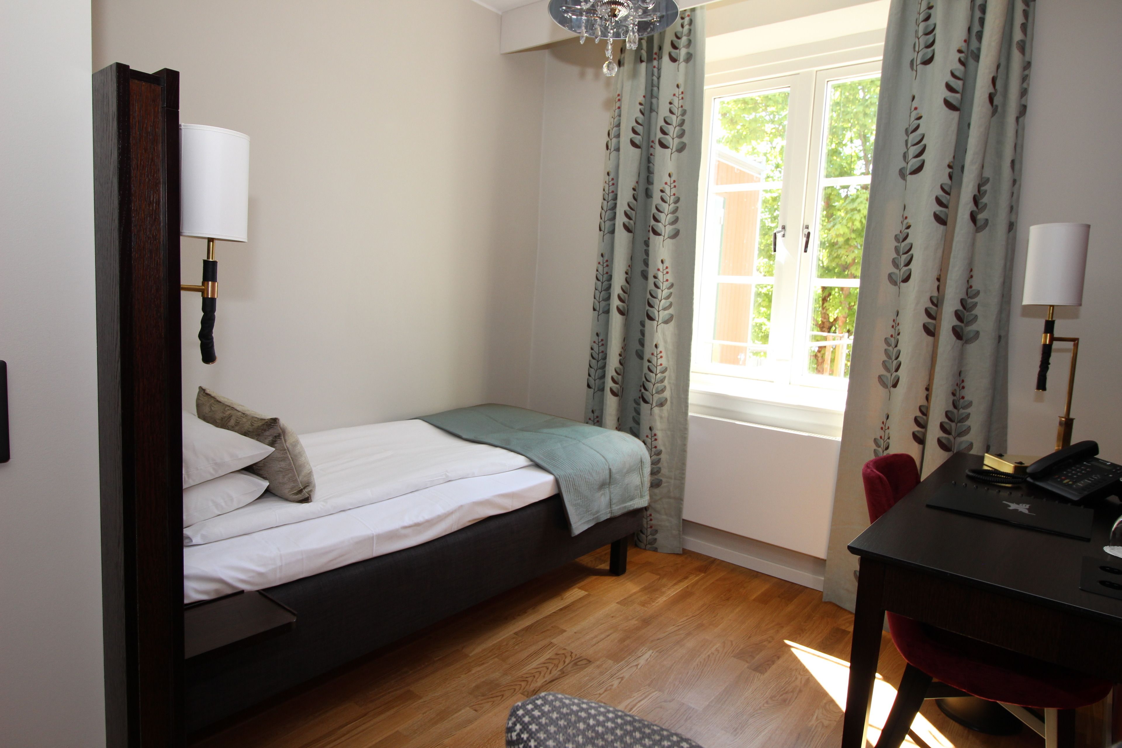 Un dormitorio con cama, escritorio, silla y ventana con cortinas.