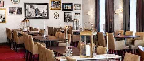 A hotel dining area with multiple tables and chairs, framed pictures on the walls, and a chandelier.