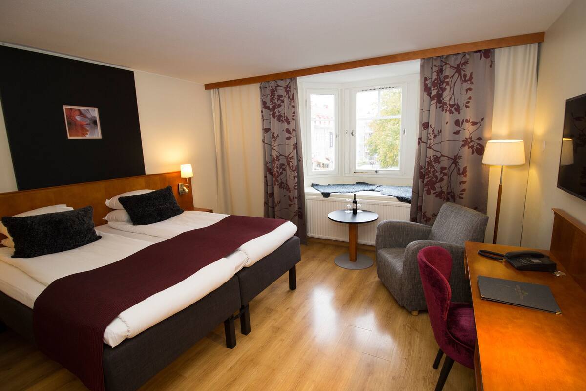A hotel room with a bed, a desk, a chair, and a small table.