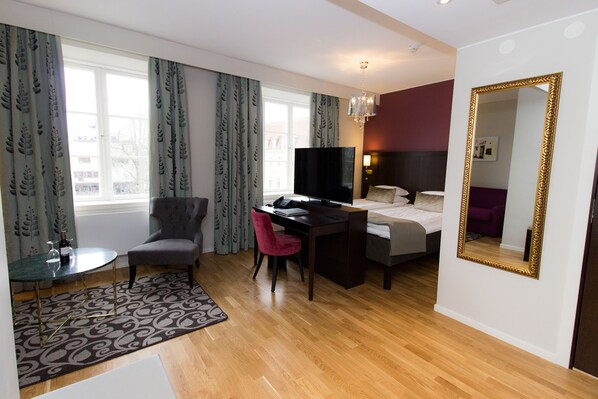 Habitación de hotel con cama, escritorio, silla, televisor y un espejo grande.