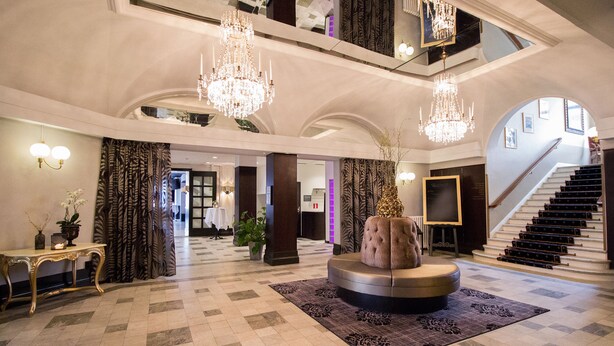 A grand lobby with a checkered floor, a central seating area, and a staircase leading to an upper level. - Grand Hotel Alingsås (Alingsas)