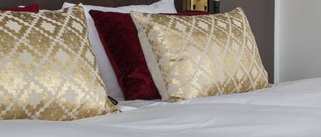 Una cama bien hecha con almohadas estampadas, una lámpara de noche y un cabecero oscuro.