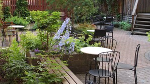 An outdoor patio with brick flooring, metal chairs, and tables. There are potted plants and a wooden bench. - Hotel Lorensberg (Gothenburg)