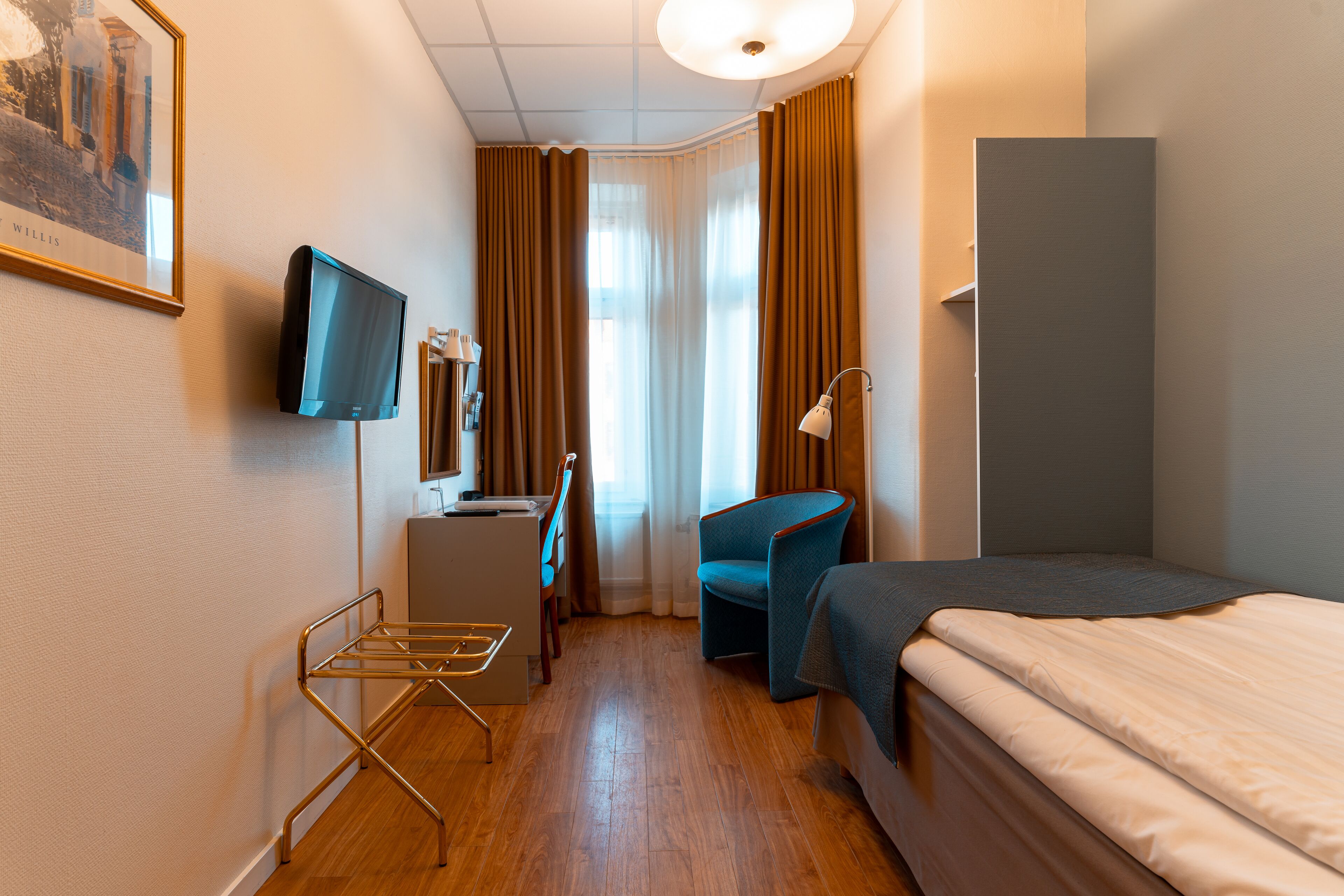 Habitación de hotel con cama, escritorio, silla, televisor y ventana con cortinas.