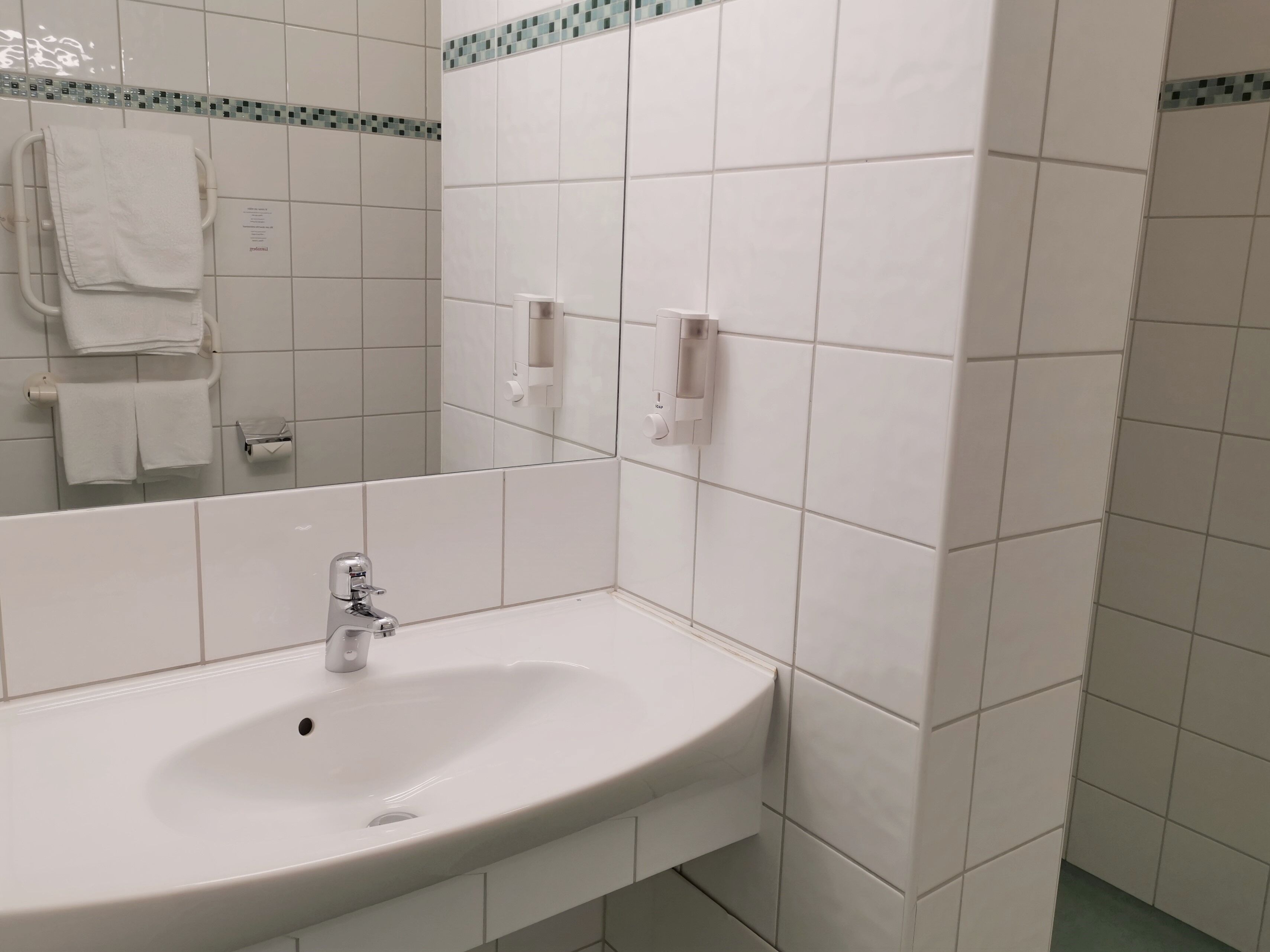 Ett badrum med ett vitt handfat, en spegel och en handdukshängare.