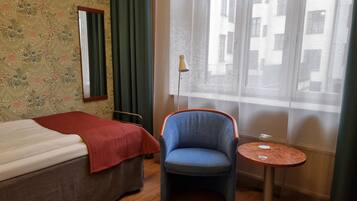 A hotel room with a bed, a chair, a small table, and a window with curtains.
