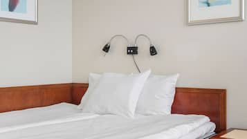 Cama bem arrumada com lençóis brancos, cabeceira de madeira e mesa de cabeceira com abajur.