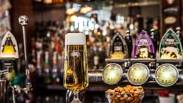 A glass of beer on a bar counter with beer taps and a bowl of nuts in the foreground.
