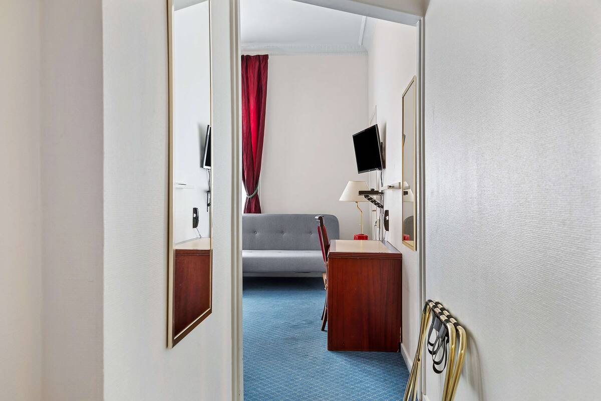 Habitación de hotel con cama, escritorio, silla, televisor y ventana con cortina roja.