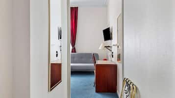 A hotel room with a bed, a desk, a chair, a TV, and a window with a red curtain.