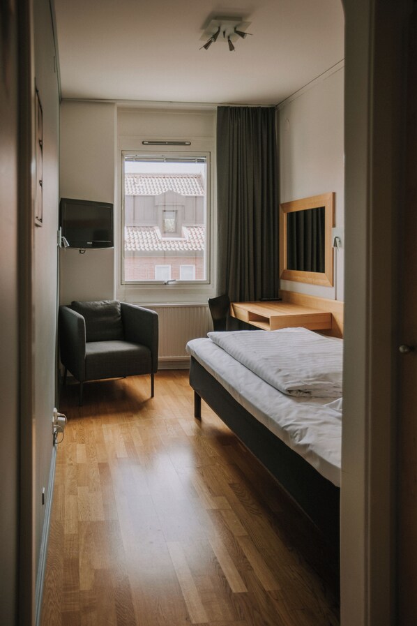 A bedroom with a bed, a chair, a desk, a television, and a window with curtains.