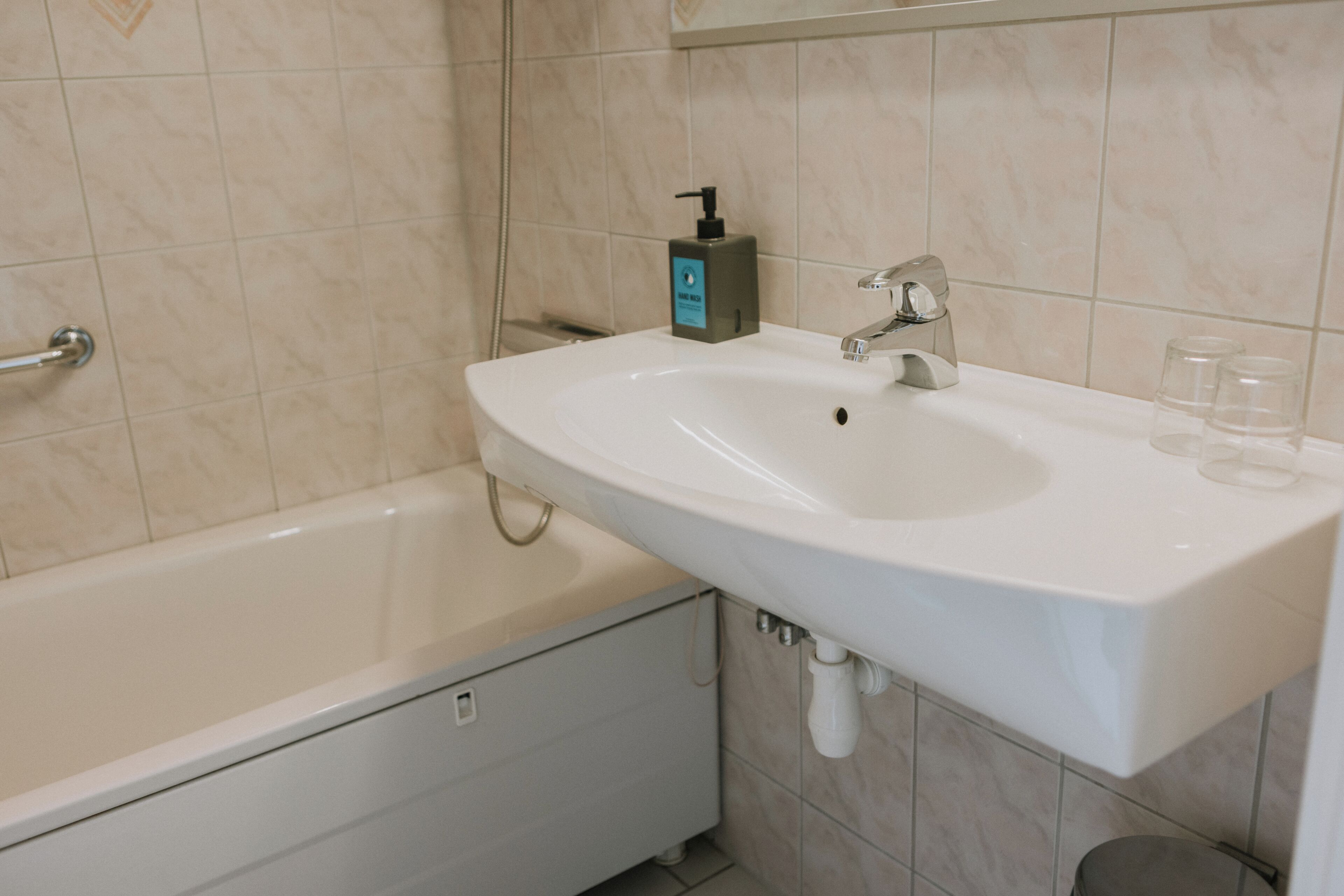 Un baño con un lavabo blanco, grifo y una botella de jabón para manos.