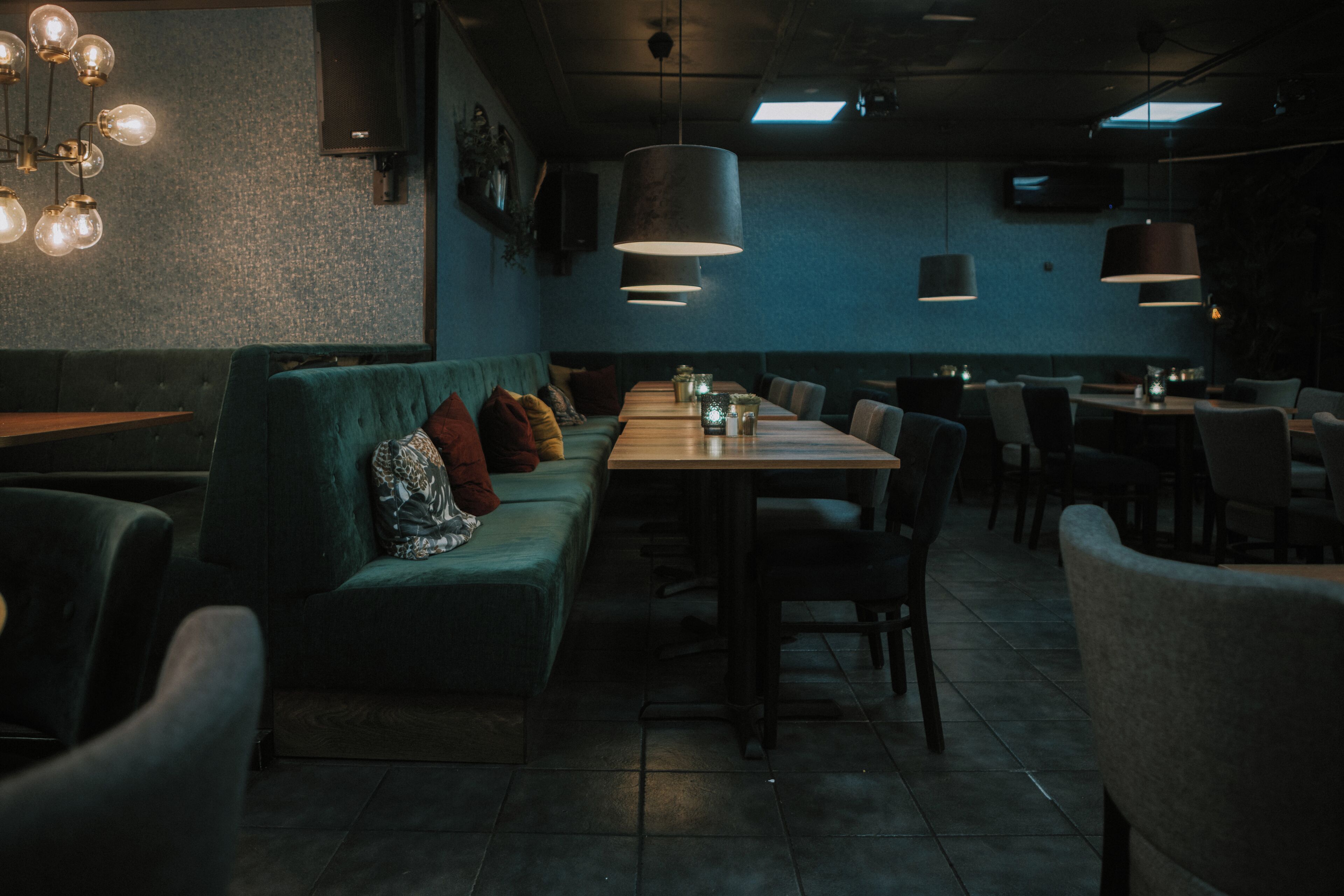 Un ristorante con un lungo tavolo, sedute imbottite, luci a sospensione e una parete strutturata.