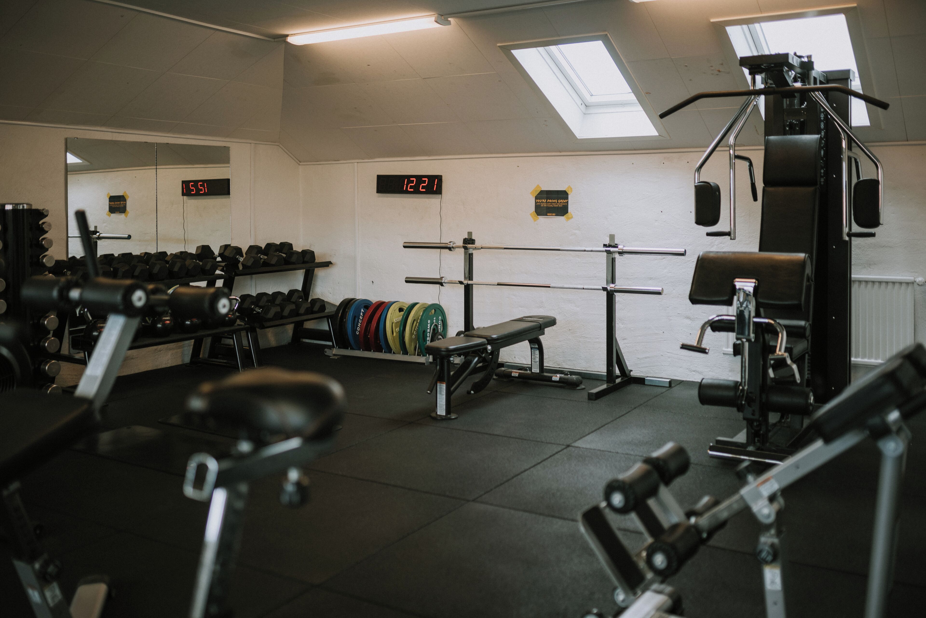 Een sportschool met gewichthefapparatuur, een bank en een spiegelwand.