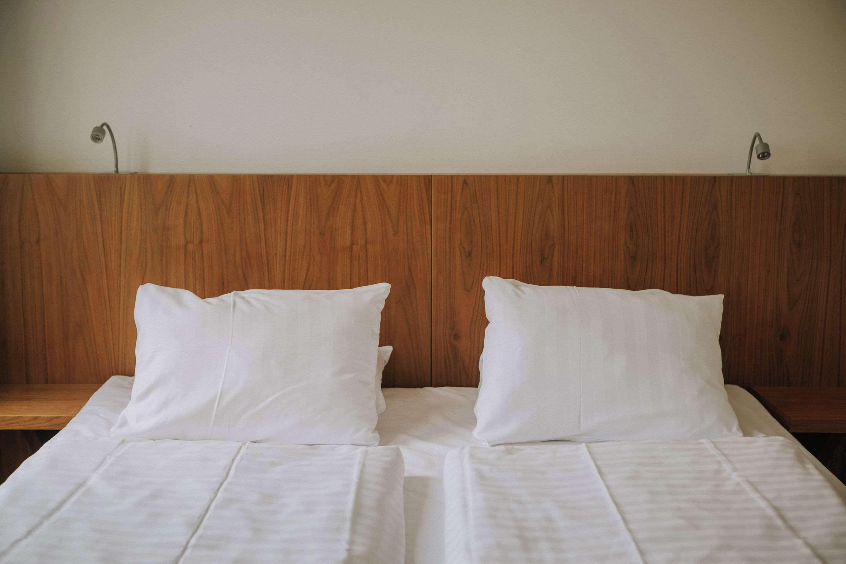 A double bed with white linens and two pillows, a wooden headboard, and two bedside lamps.
