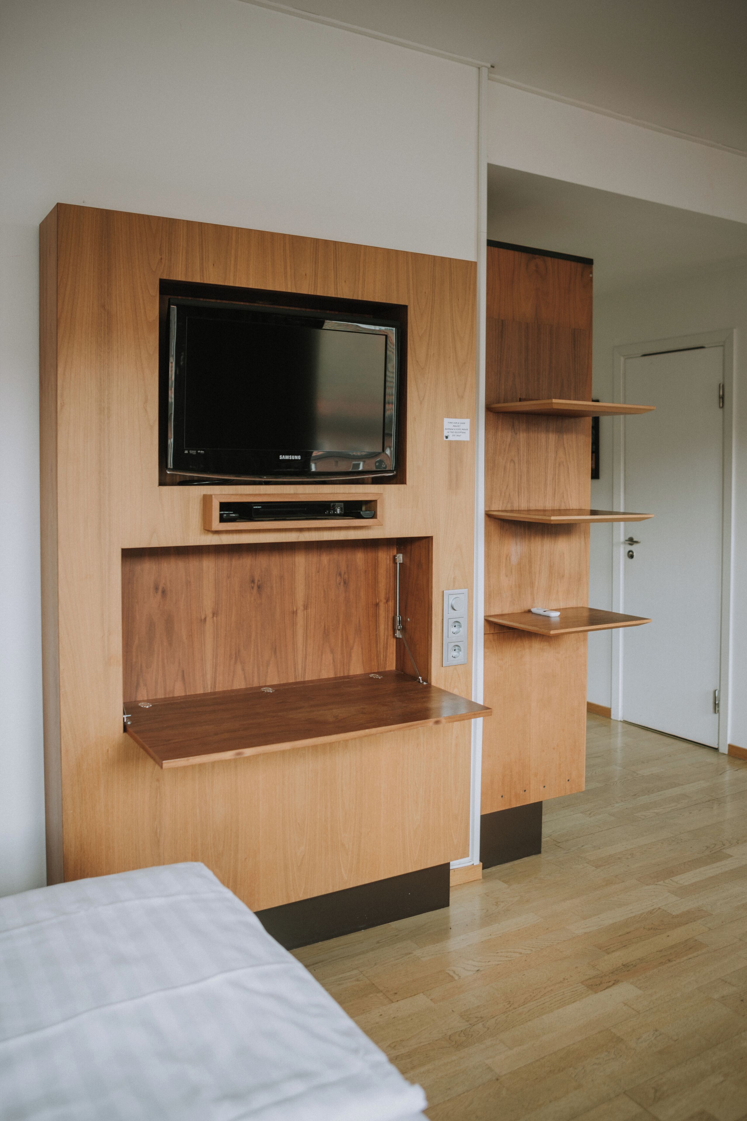 A modern room with a built-in TV, wooden shelves, and a bed.