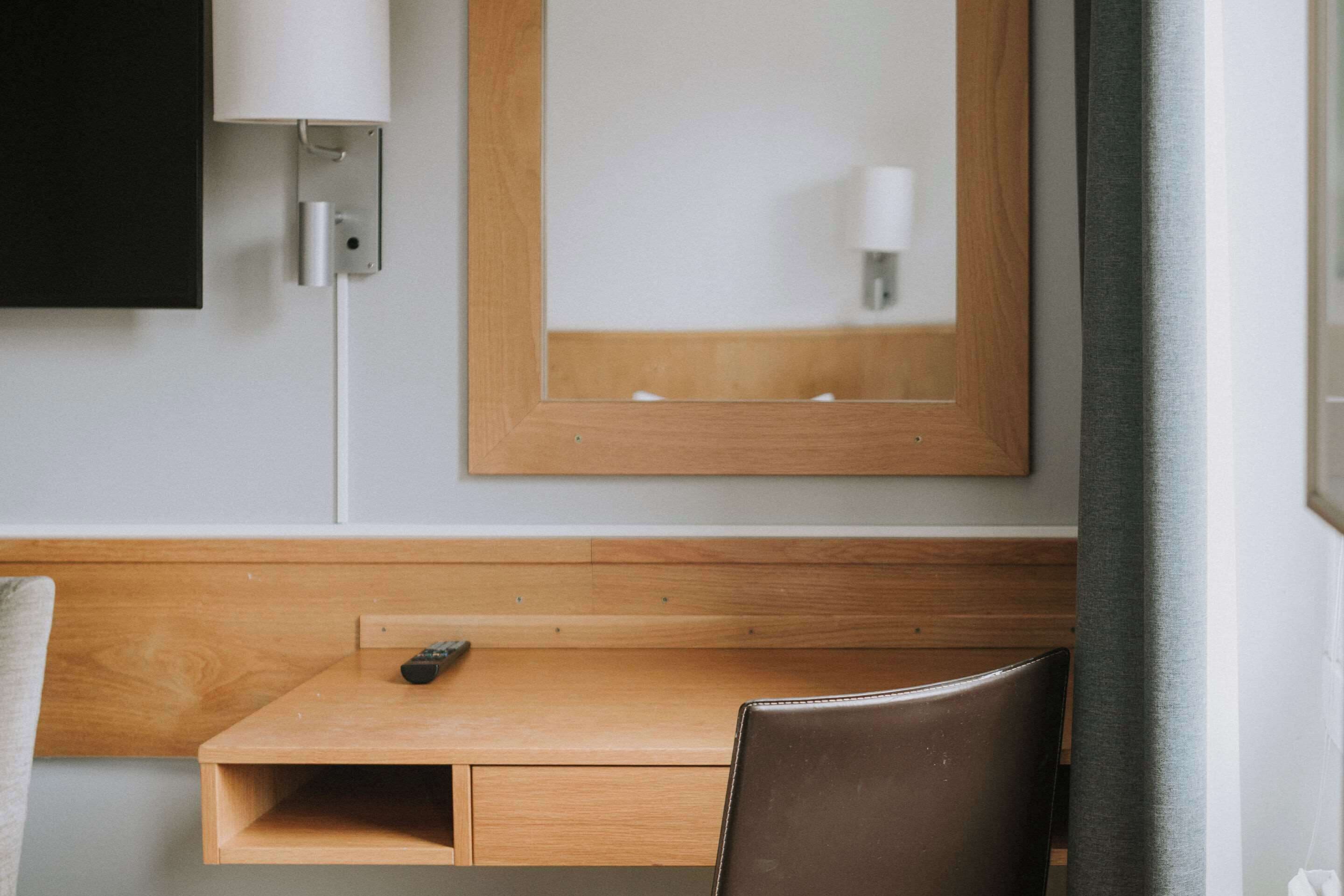 Une chambre d’hôtel avec un bureau en bois, une chaise, un téléviseur fixé au mur et un miroir au-dessus du bureau.