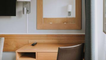 Une chambre d’hôtel avec un bureau en bois, une chaise, un téléviseur fixé au mur et un miroir au-dessus du bureau.