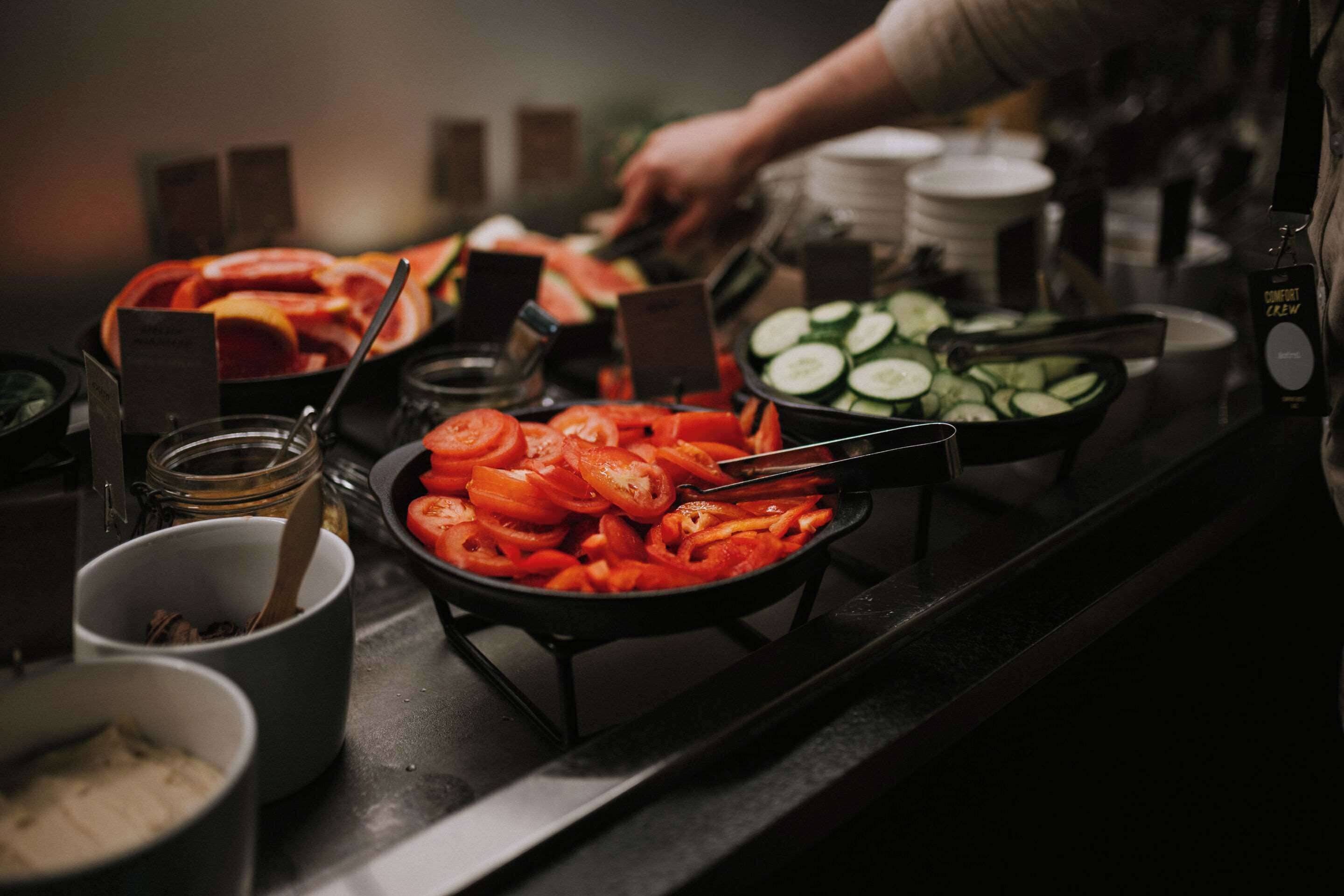 A buffet with various food items including sliced tomatoes, cucumbers, and carrots.