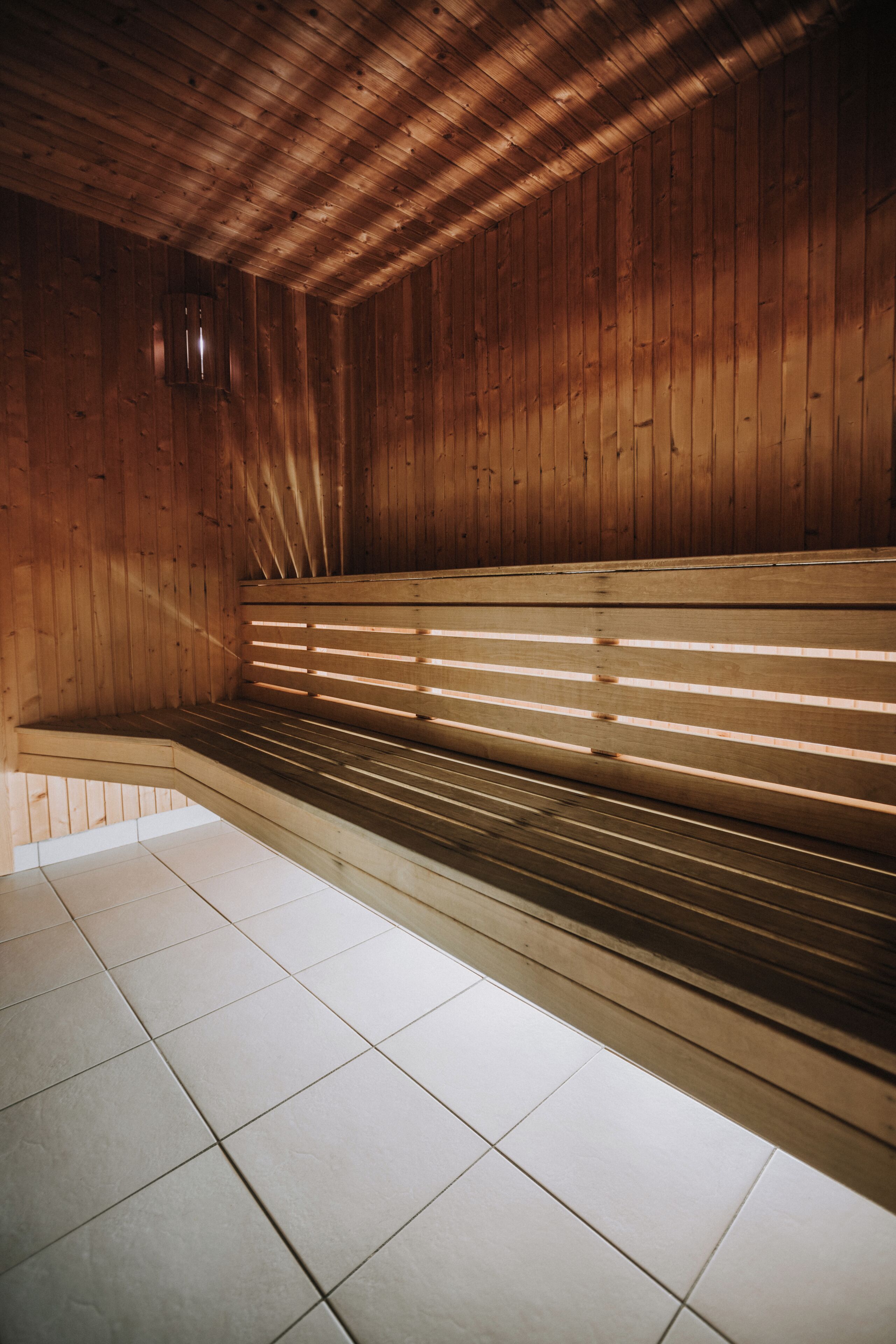 Una sauna con paredes y bancos de madera, piso de baldosas y una lámpara visible.